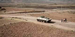 People in Tigray region walk near an abandoned tank 