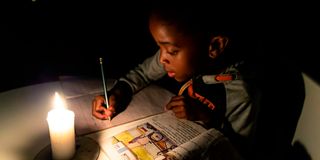 A Zimbabwean boy does his homework using a candle. 