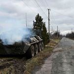 A Ukrainian serviceman walks past a burning APC