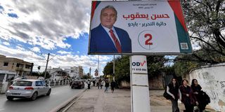 Tunisian women walk underneath an electoral billboard