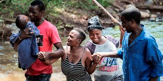 A woman with her baby is helped to cross River Mhlambanyatsi 