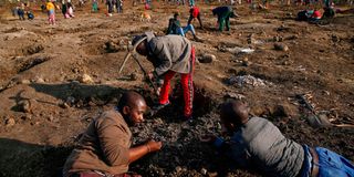 A man uses a pick axe to dig as others search for what they believe to be diamonds