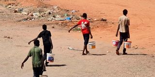 Youths carry buckets of water in Khartoum